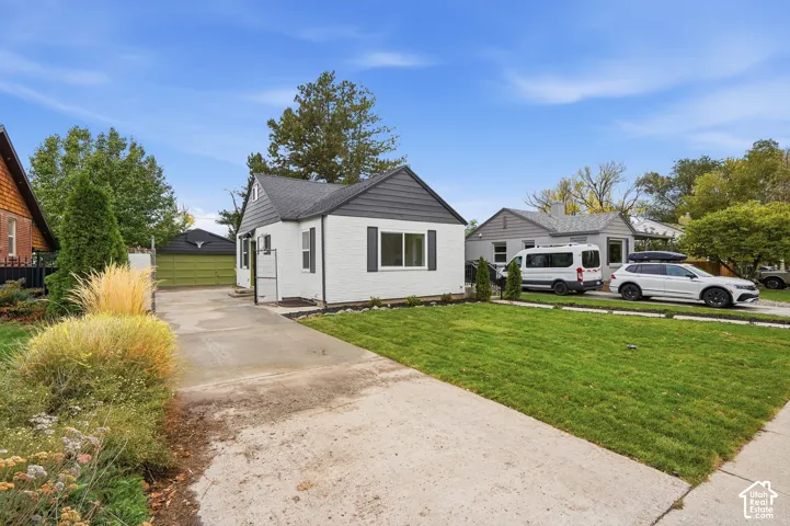 Single-story exterior featuring painted brick siding, asphalt shingle roofing, decorative shutters, a concrete driveway, and a detached garage
