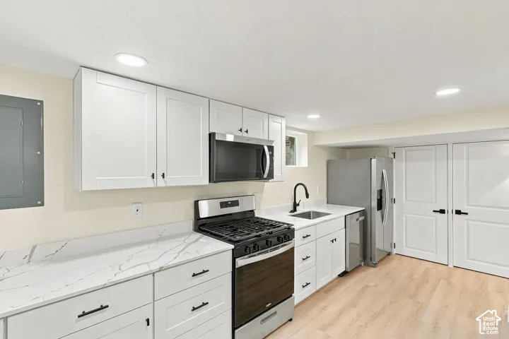 Kitchen featuring white shaker-style cabinetry, white countertops with grey veining, stainless steel appliances, a matte black kitchen faucet, and light-tone wood-finish flooring