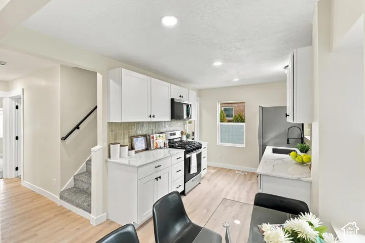 Kitchen featuring white shaker-style cabinetry, stone-look countertops, patterned tile backsplash, stainless steel appliances, and wood-finish flooring