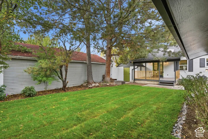 Backyard featuring a manicured lawn, covered wood-deck patio with railing, mature trees, and grey horizontal siding