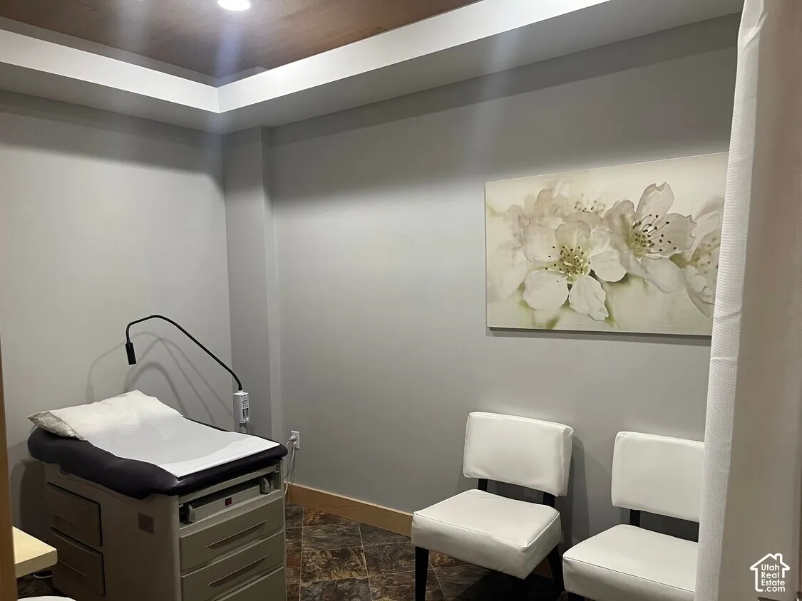 Recessed tray ceiling with warm wood-tone paneling, stone-finish flooring, and neutral wall color