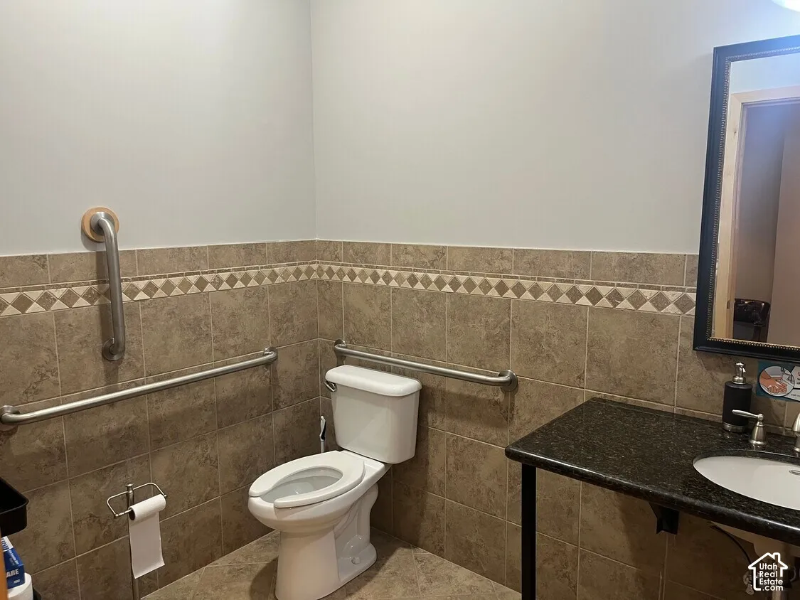 Bathroom featuring wall-mounted stainless steel grab bars, full-height tile wainscoting with decorative accent border, stone-finish countertop, and undermount sink