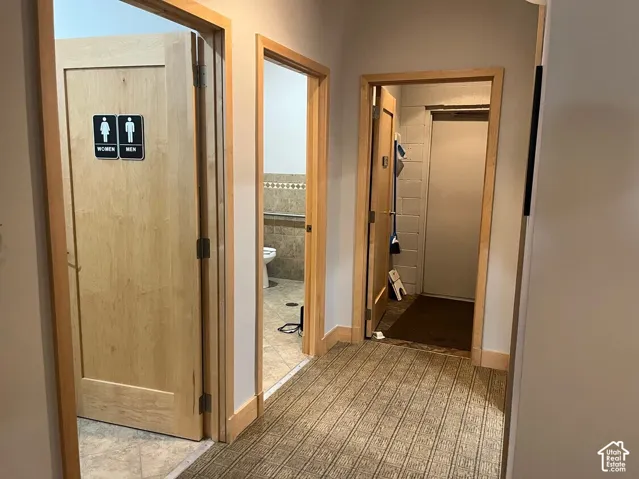 Hallway featuring natural wood-finish door frames, patterned carpeting, and multiple interior doors