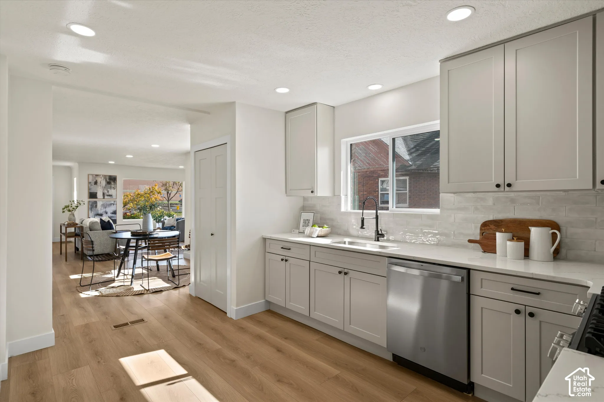 Kitchen featuring shaker-style cabinetry, solid-surface countertops, textured brick-pattern backsplash, stainless steel dishwasher, and wood-finish flooring