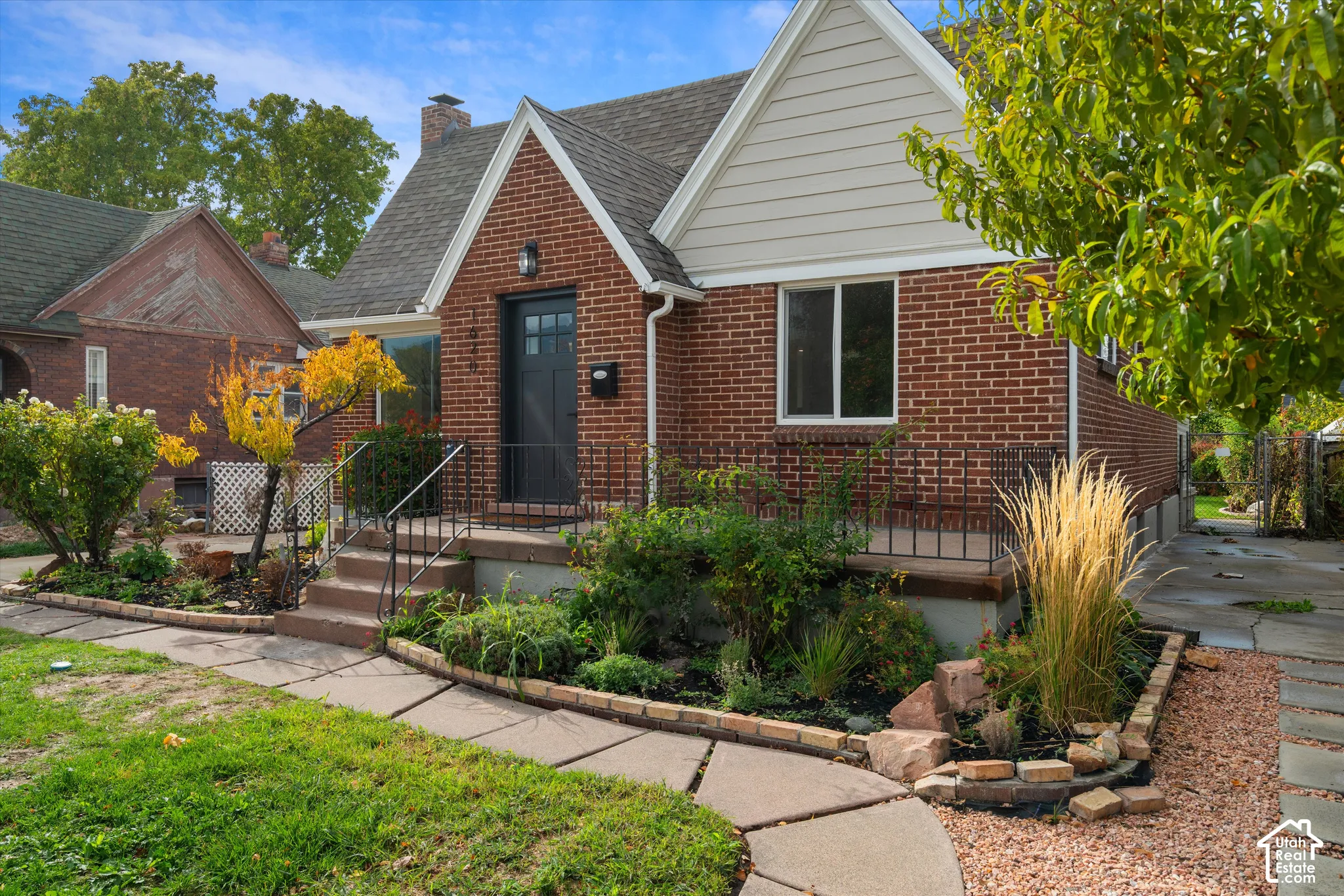 Traditional brick exterior featuring a steeply pitched roofline, horizontal siding accents, front porch with wrought-iron railing, and a stone-paver walkway