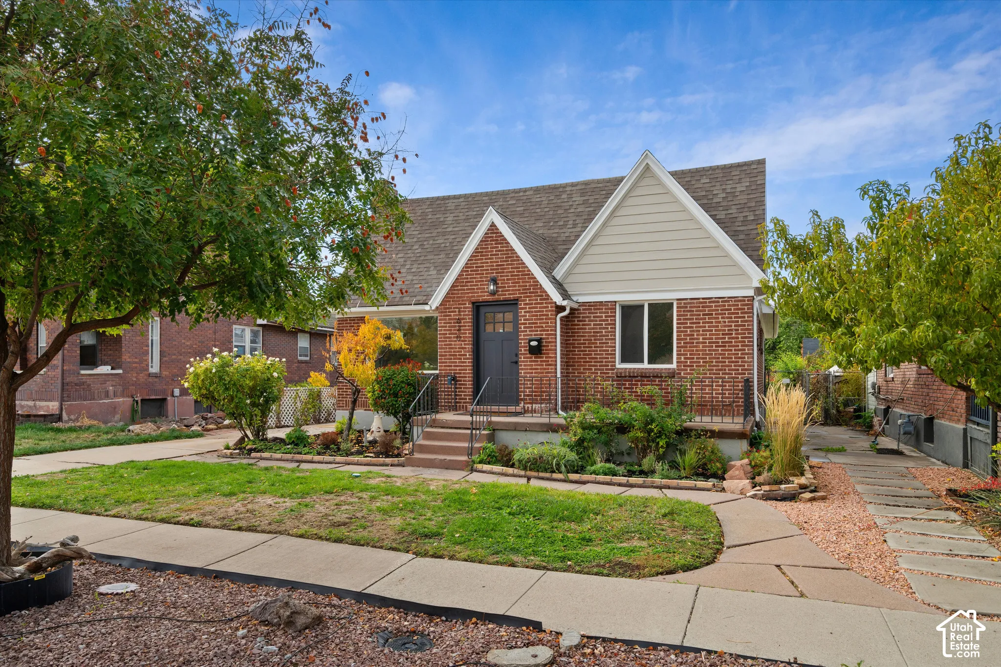 Brick exterior featuring dual gables, horizontal siding accents, an elevated front porch with wrought iron railing, and a concrete paver walkway