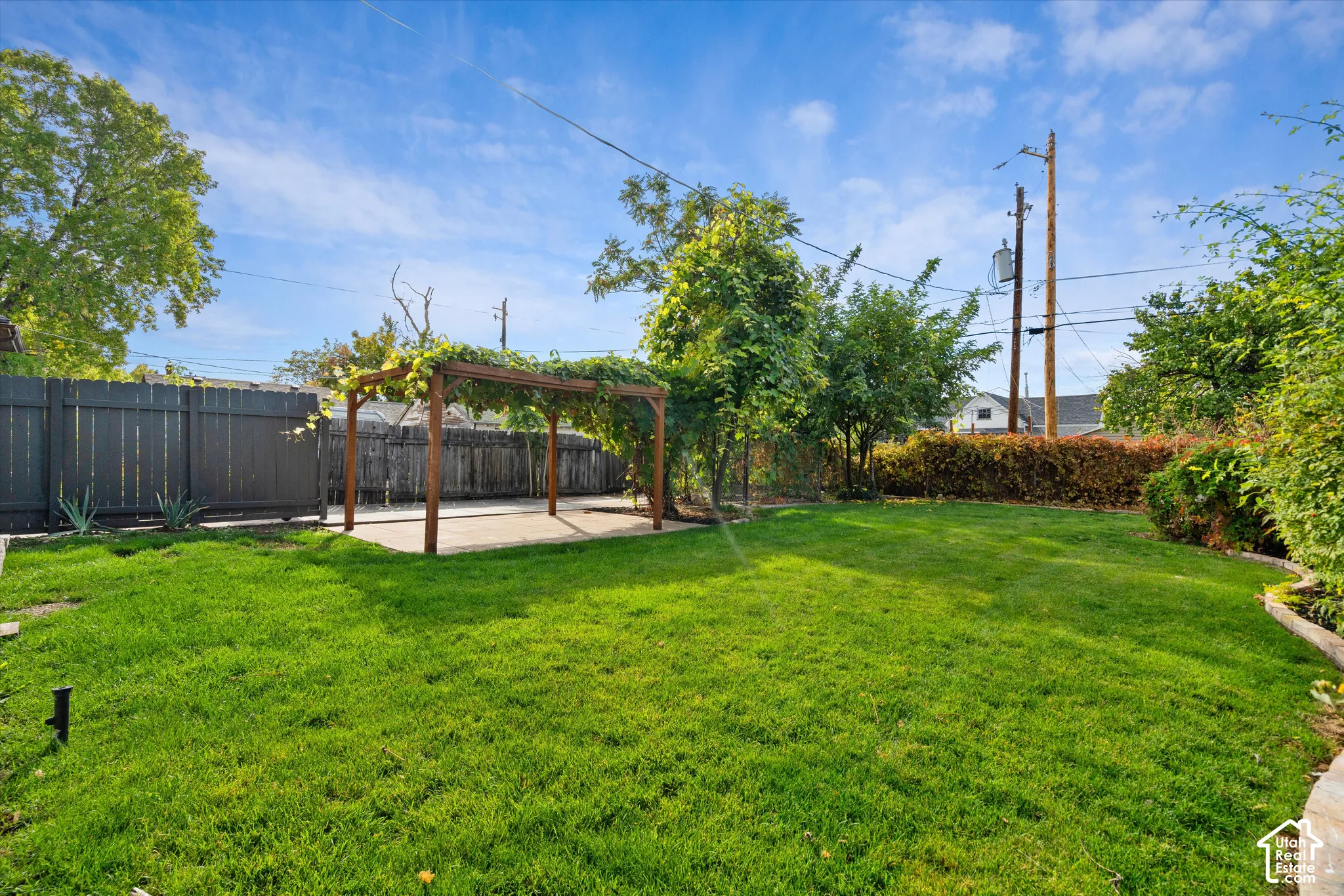 Backyard featuring a grass lawn, a wood-frame pergola, perimeter wood fencing, and mature trees