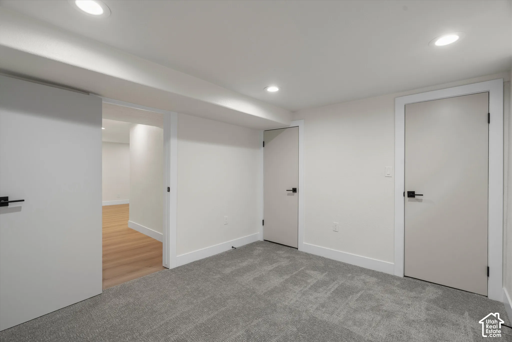 Interior space featuring recessed lighting, grey carpeting, neutral wall finishes, solid-core doors with matte black hardware, and wood-finish flooring