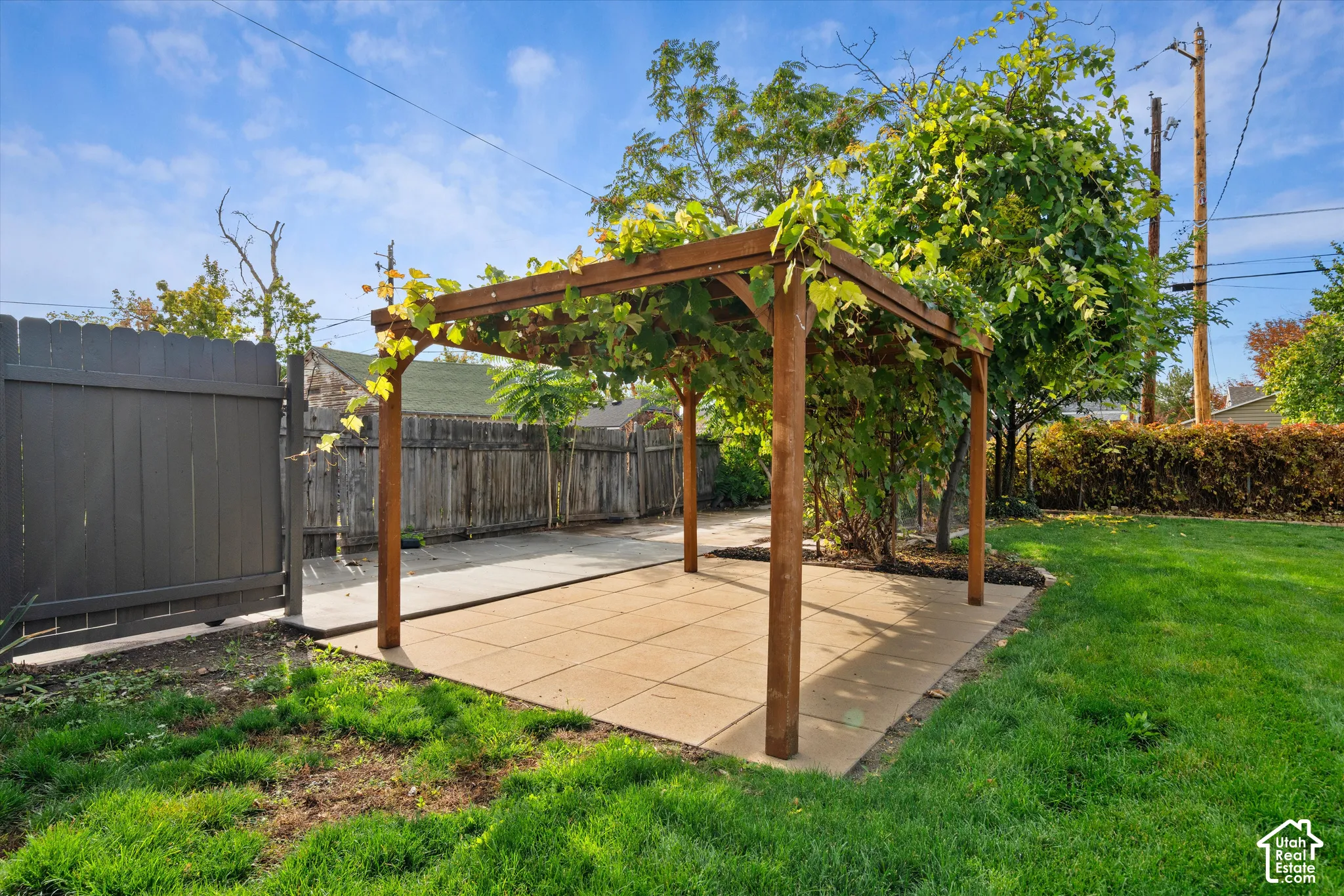 Outdoor living area featuring a wooden pergola, square paver patio, mature vine foliage, and privacy fencing
