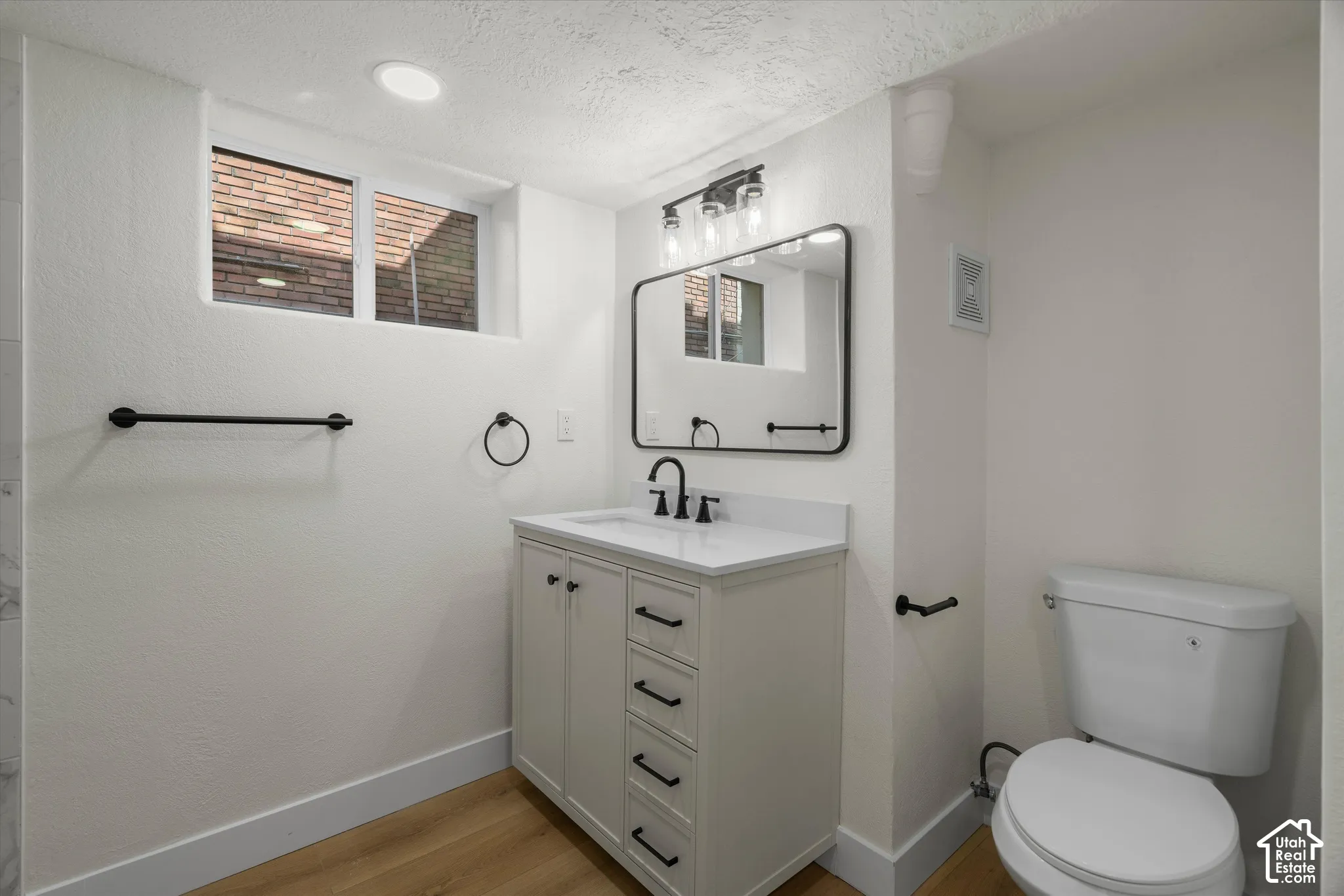 Bathroom featuring a vanity with a white countertop, rectangular under-mount sink, matte black hardware, framed rectangular mirror, and wood-finish flooring