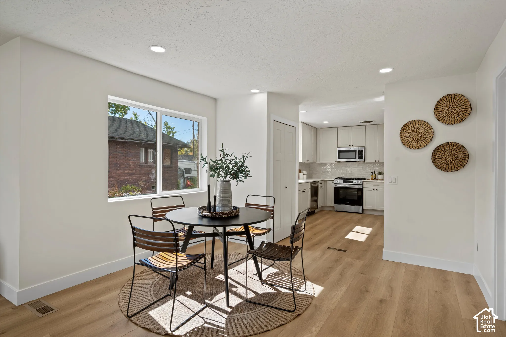 Open-concept kitchen and dining area featuring wood-finish flooring, recessed lighting, neutral wall palette, and cabinetry with stainless steel appliances