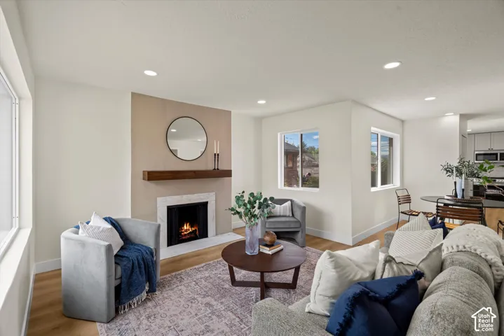 Fireplace featuring a stone surround, wood-finish mantel, and neutral-toned accent wall, complemented by recessed lighting and wood-finish flooring