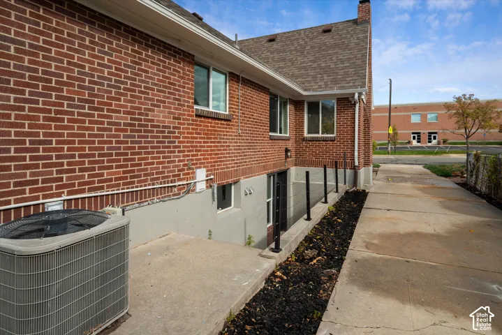 Brick exterior featuring asphalt shingle roofing, concrete side walkway, and subterranean stairwell access with metal railing