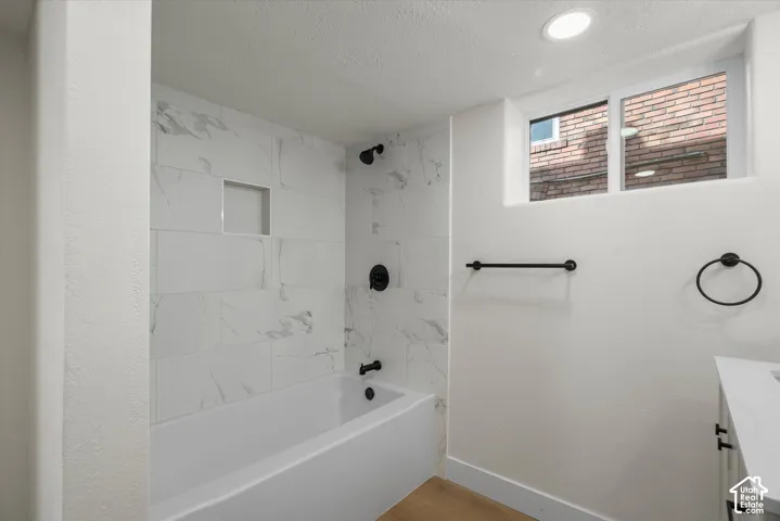 Bathroom featuring a white bathtub, floor-to-ceiling tile surround with marble-finish detailing, built-in recessed wall niche, matte black plumbing fixtures, and a horizontal sliding window