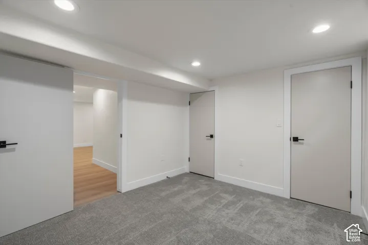 Interior space featuring recessed lighting, grey carpeting, neutral wall finishes, solid-core doors with matte black hardware, and wood-finish flooring
