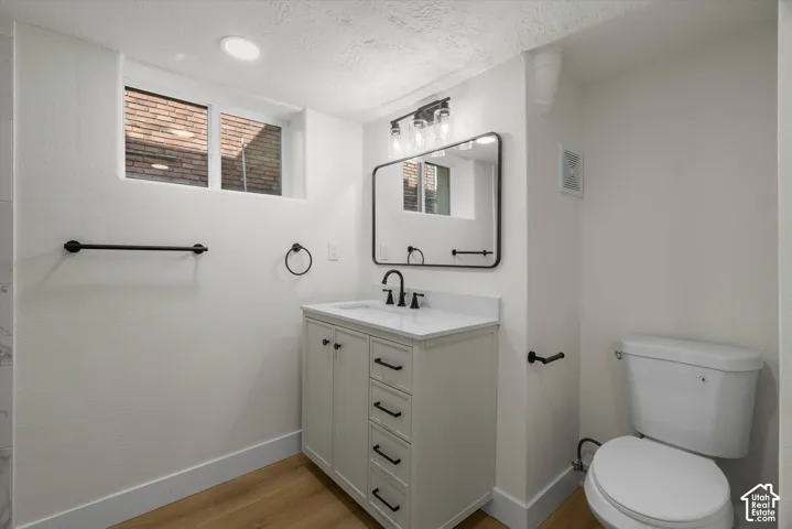 Bathroom featuring a vanity with a white countertop, rectangular under-mount sink, matte black hardware, framed rectangular mirror, and wood-finish flooring