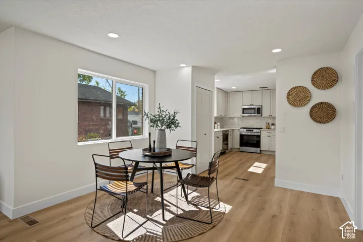 Open-concept kitchen and dining area featuring wood-finish flooring, recessed lighting, neutral wall palette, and cabinetry with stainless steel appliances