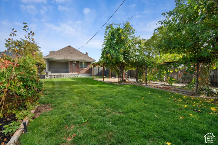 Backyard featuring a manicured lawn, brick exterior siding, a covered concrete patio, and a wood-post garden trellis