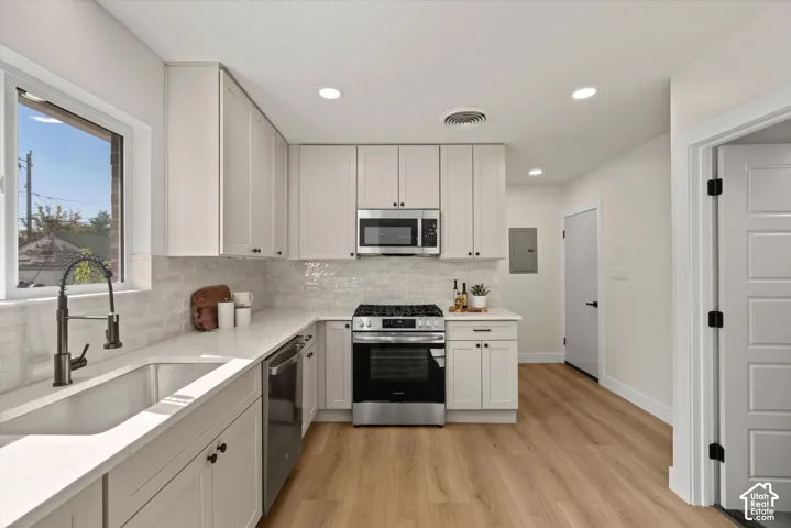 Kitchen featuring white shaker-style cabinetry, quartz countertops, subway tile backsplash, stainless steel appliances, and wood-finish flooring