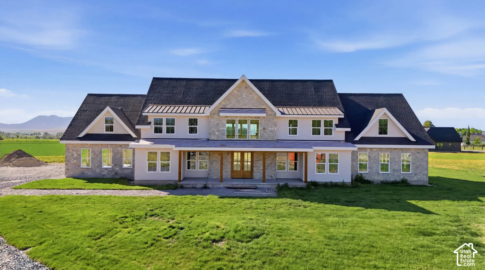 Custom residence featuring a stone and siding exterior, multiple dormer windows, metal roof accents, a covered front porch with timber posts, and a mountainous backdrop