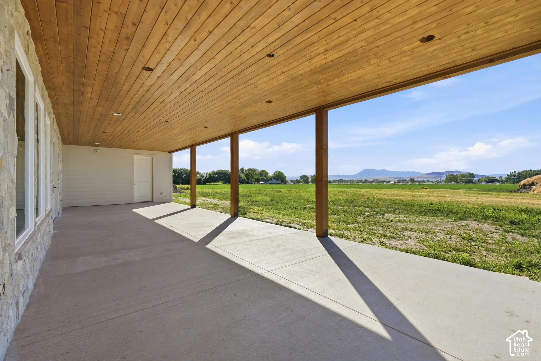 Covered concrete patio featuring a tongue-and-groove wood-plank ceiling, recessed lighting, and stone exterior cladding, overlooking mountain scenery