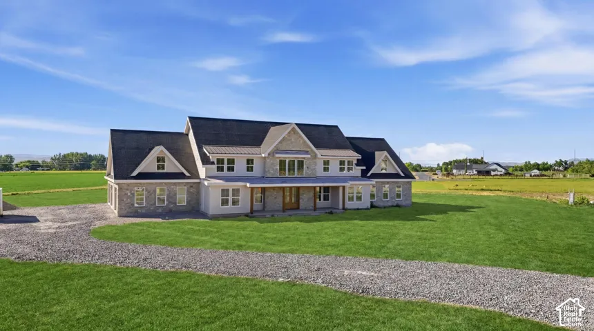 Exterior facade featuring stone veneer siding, dual-gable roofline, covered front entryway, and multi-pane windows situated on a large parcel with a gravel driveway