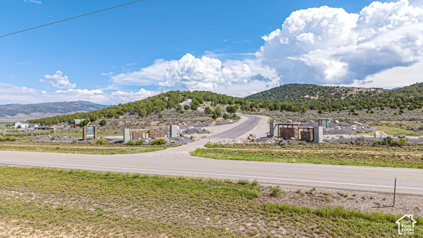 Stone and metal decorative pillars with paved entryway, mountain backdrop, and rolling landscape terrain