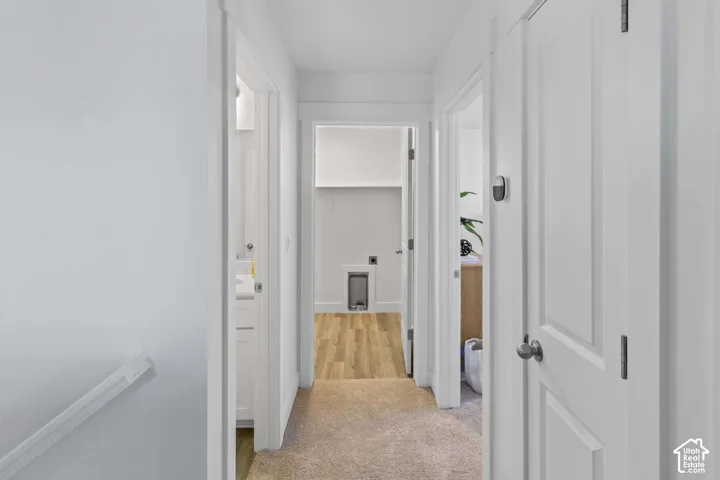 Hallway featuring neutral carpeted flooring, white six-panel doors, and wood-finish flooring in the utility area