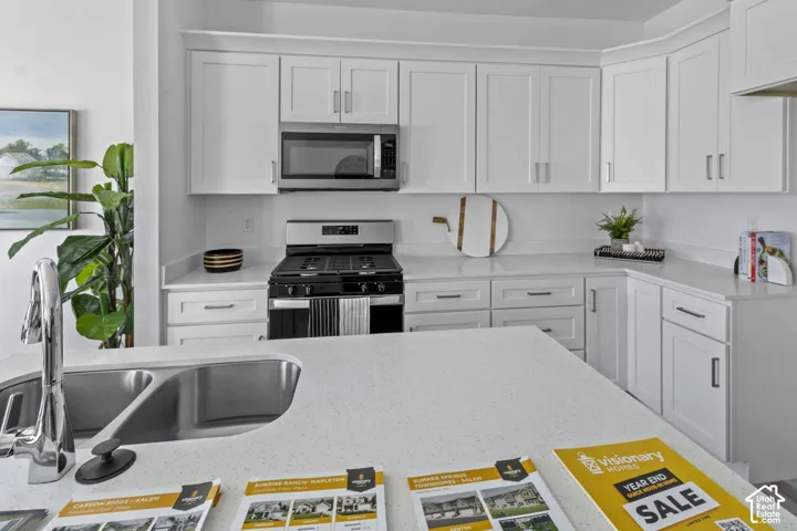 Kitchen featuring white shaker-style cabinetry, solid-surface countertops, a stainless steel double-basin sink with a chrome high-arc faucet, and stainless steel appliances