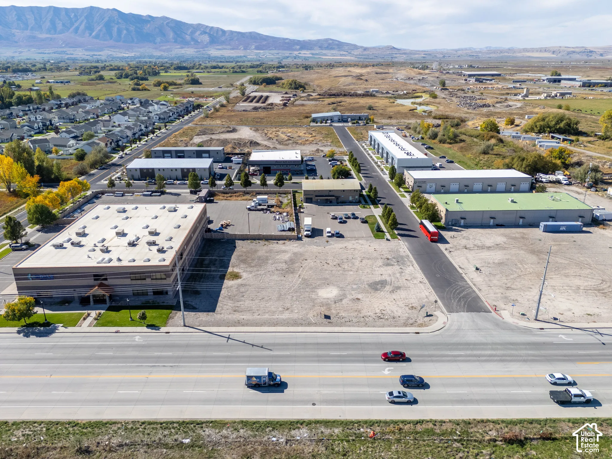 Industrial property complex featuring multiple multi-unit warehouses, a large detached office building, expansive asphalt parking areas, and prominent mountain backdrops