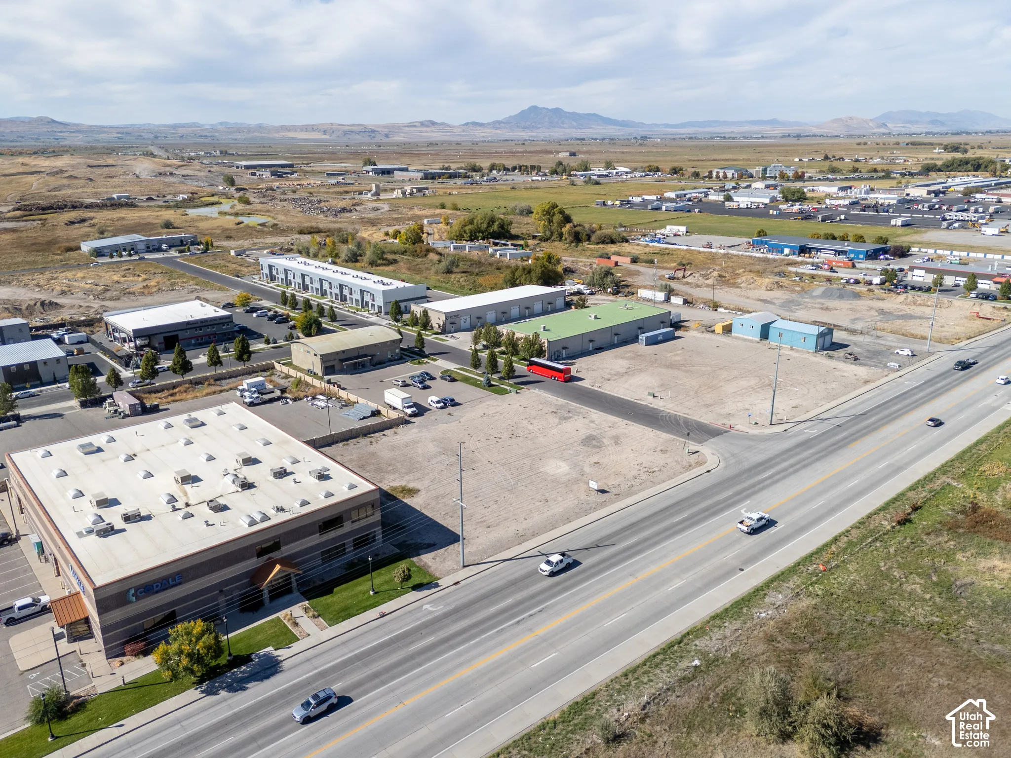 Aerial perspective of a commercial lot with frontage on a primary roadway, featuring a flat building site, expansive horizon, and mountain topography