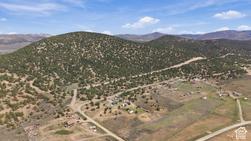 Aerial perspective featuring expansive topography, mountainous terrain, native vegetation, and unpaved roadway access