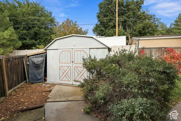 Detached metal storage shed with double-door entry, concrete pad, and side lean-to structure, enclosed by perimeter fencing