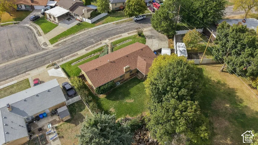 Aerial perspective of a property featuring a corner lot, asphalt-shingled roof, masonry chimney, and expansive lawn with mature trees