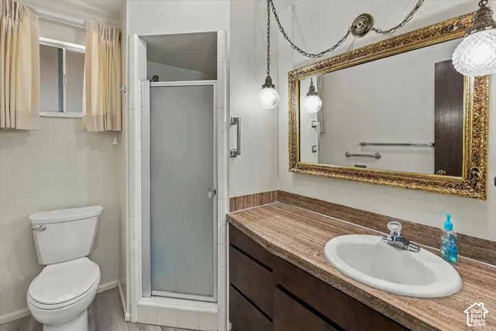 Bathroom featuring a vanity with wood-finish cabinetry, stone-texture countertop, inset sink, integrated shower enclosure with glass door, and wall-mounted light fixtures