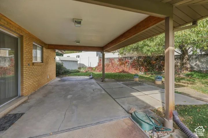 Covered concrete patio featuring a brick exterior wall, structural wood beam support, and sliding glass door