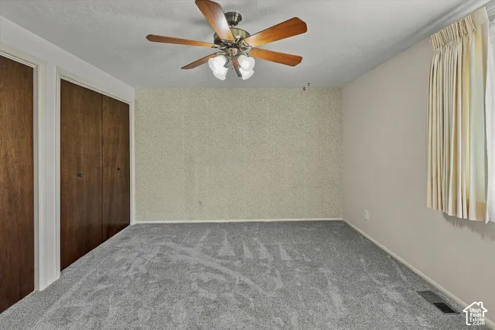 Neutral wall tones paired with textured accent wall, integrated ceiling fan with multi-light fixture, and wood-finish closet doors
