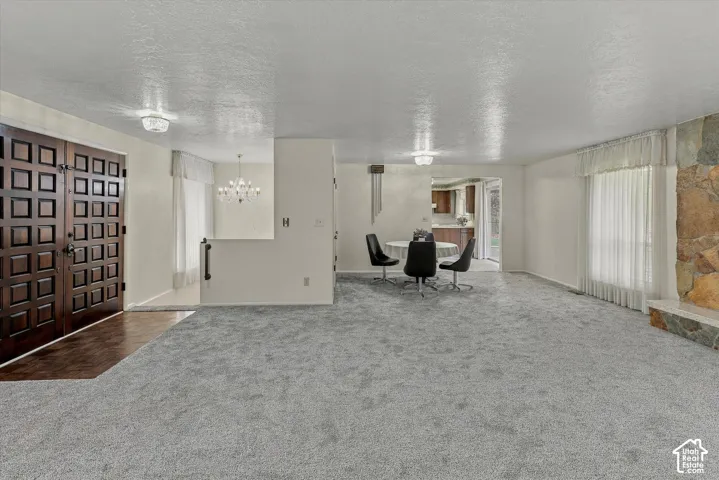 Double-door wooden entryway, natural stone fireplace surround, neutral carpeting, and multi-arm chandelier lighting