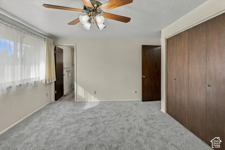 Neutral wall-to-wall carpeting, ceiling fan with multi-light fixture, and dual wood-finish closet doors