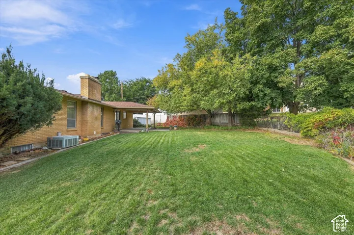 Expansive backyard featuring a brick exterior, covered patio, manicured lawn, and mature trees