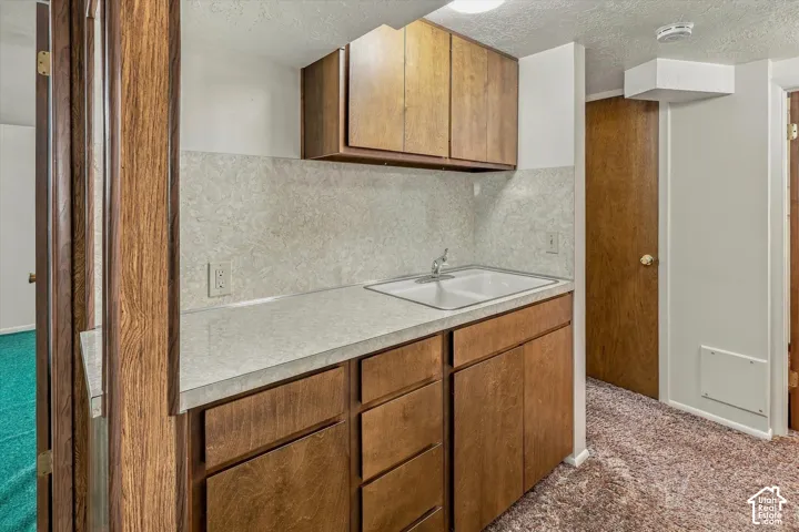 Wet bar featuring wood cabinetry, laminate countertops, a dual-basin sink, and a matching laminate backsplash