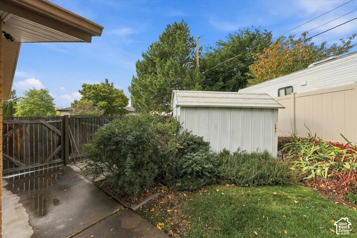 Outdoor space featuring a concrete patio, wood privacy fencing, a storage shed, and mature landscaping