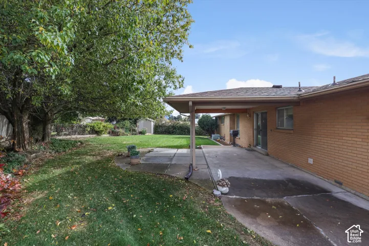 Spacious backyard featuring a brick exterior, concrete patio, covered porch, mature trees, and a storage shed