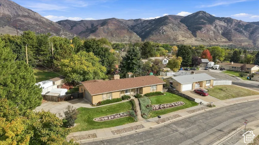 Rambler-style residence featuring a brick facade, asphalt shingle roof, attached garage, terraced garden beds, and mountain backdrop