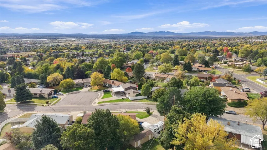 Aerial view of the surrounding residential neighborhood featuring mature deciduous trees and mountainous terrain on the horizon