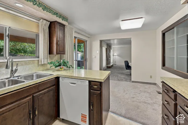 Kitchen featuring dark-finish wood cabinetry, integrated dishwasher, dual-basin stainless steel sink with high-arch faucet, laminate countertops, and built-in glass-front display cabinetry