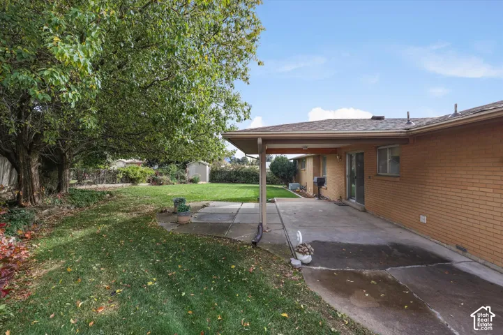 Brick exterior, covered concrete patio, and expansive backyard featuring mature trees