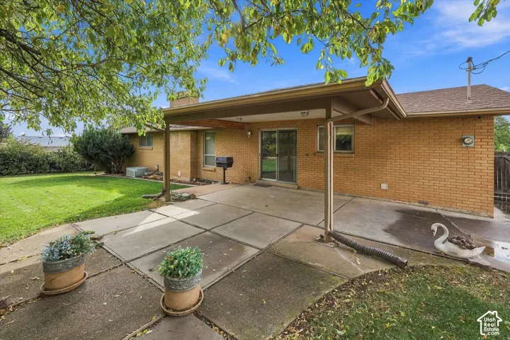 Brick exterior featuring a covered concrete patio, sliding glass door, and expansive backyard with mature trees