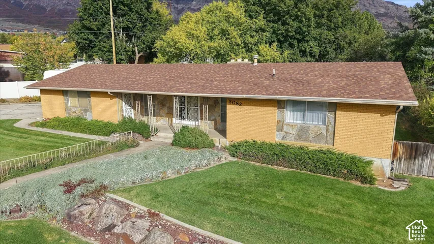 Single-story exterior featuring tan brick siding, stone facade accents, an asphalt shingle roof, and mountain backdrop