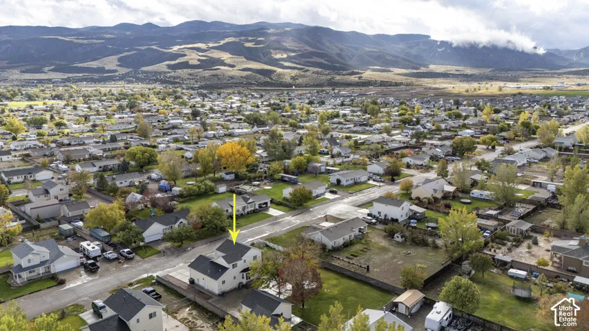 Aerial perspective of a multi-level residence featuring a pitched roof, concrete driveway, and expansive mountain backdrop
